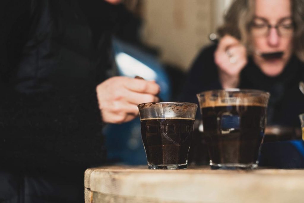 Close up of two glasses with coffee standing on wooden table, people in background.