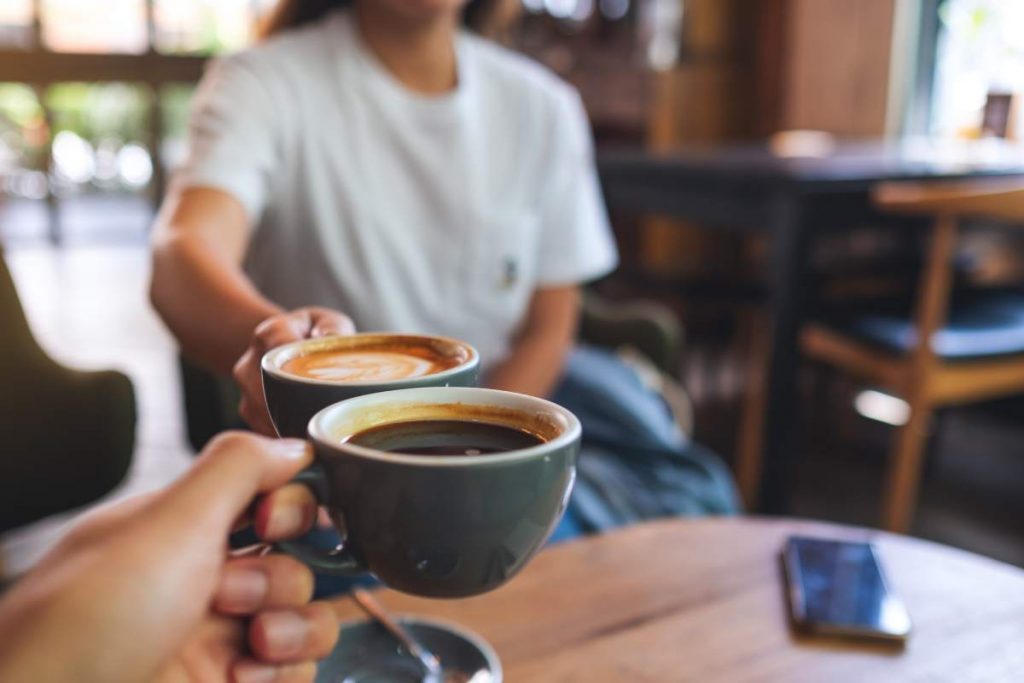 Closeup image of a man and a woman clinking coffee mugs in cafe