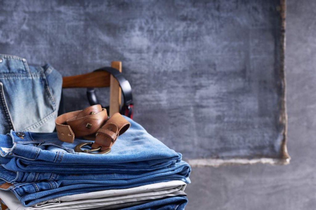 Denim jeans and jacket with belt at old wooden chair near wall background texture. Modern casual style of classic jeans fashion