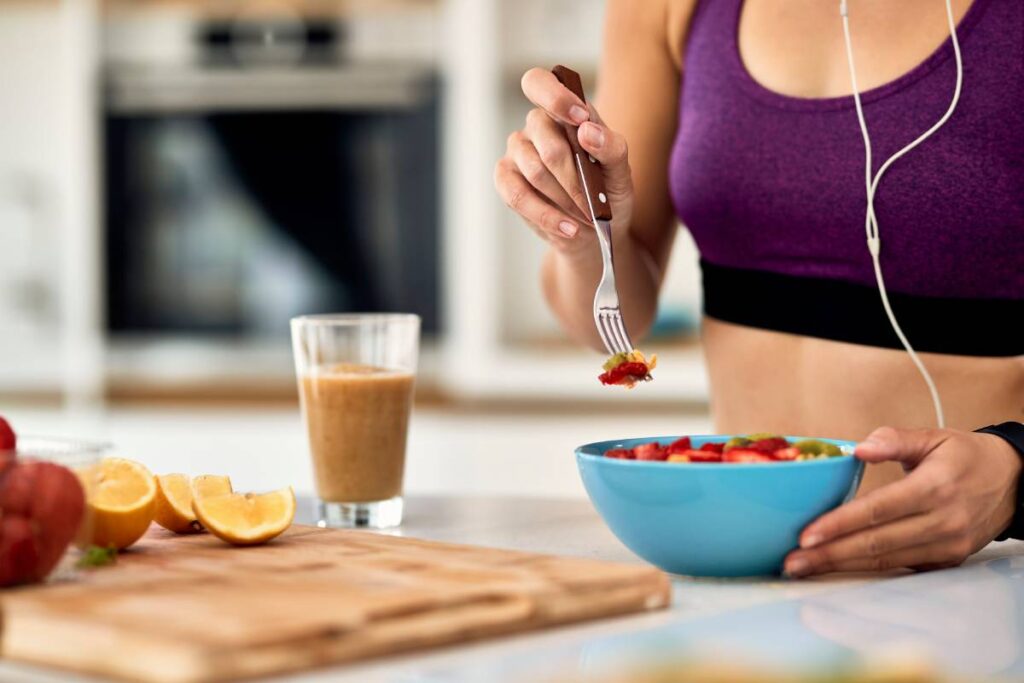 Close-up of female athlete having fruit salad for a snack in the kitchen. Discover why eating before a workout is essential, what types of foods provide the best energy and muscle support, and how timing your meals can improve performance and recovery.